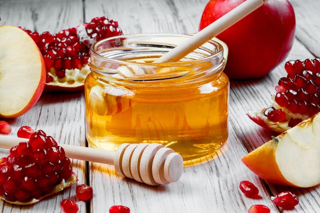 Jar with honey apples and pomegranates on white wooden background Happy Rosh Hashanah