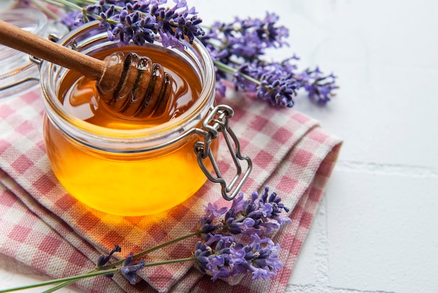 Jar with honey and fresh lavender flowers on a white tile background