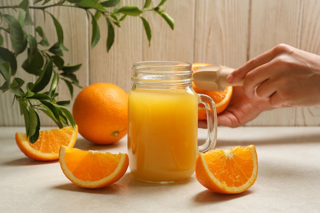 Jar with orange juice against wooden with female hand hold juicer and orange