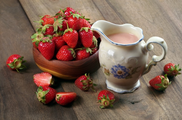 jar with strawberry milk, ripe strawberries in a wooden bowl on a wooden table