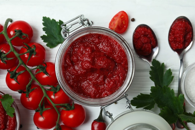 Jar with tomato paste on white wooden surface with ingredients