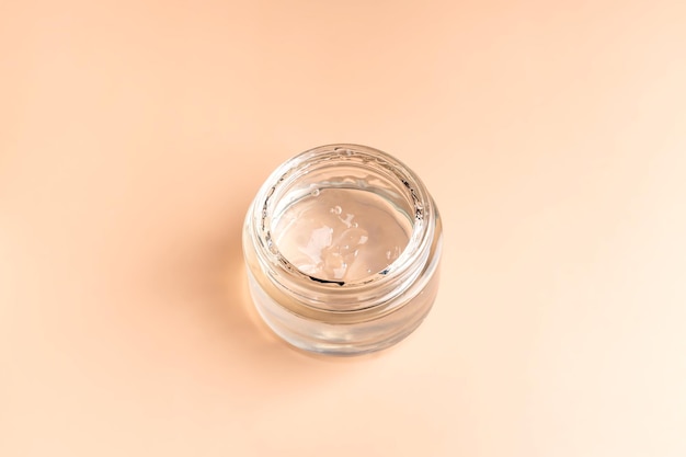 Jar with transparent cosmetic product gel or cream on beige pastel background Unbranded package with an antioxidant cream for selfcare View from above