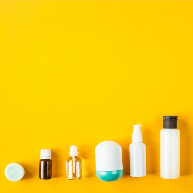 Jars and containers with cosmetic products are lined in a row on a yellow background. 