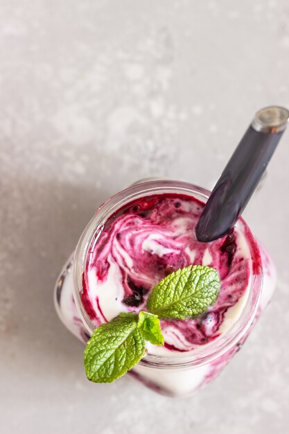 Jars of natural yogurt with berry sauce and mint on light grey table. Healthy eating. Copy space. Summer food concept. 