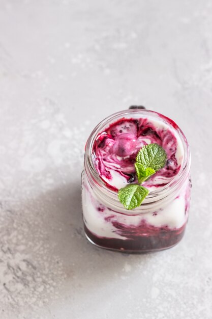 Jars of natural yogurt with berry sauce and mint on light grey table. Healthy eating. Copy space. Summer food concept. 