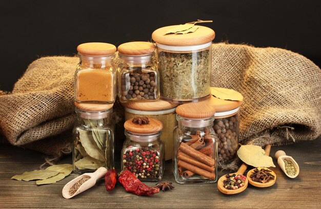 Jars and spoons with spices on wooden table on black background