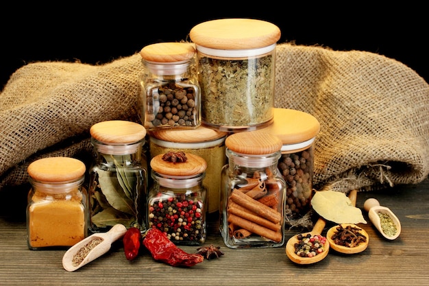 Jars and spoons with spices on wooden table on black background