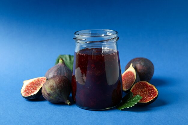 Jars with fig jam and ingredients on blue background