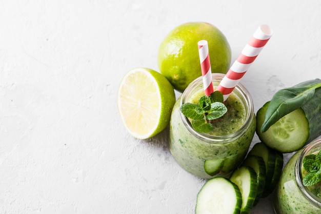 Jars with green smoothie and red tubules on a light background.