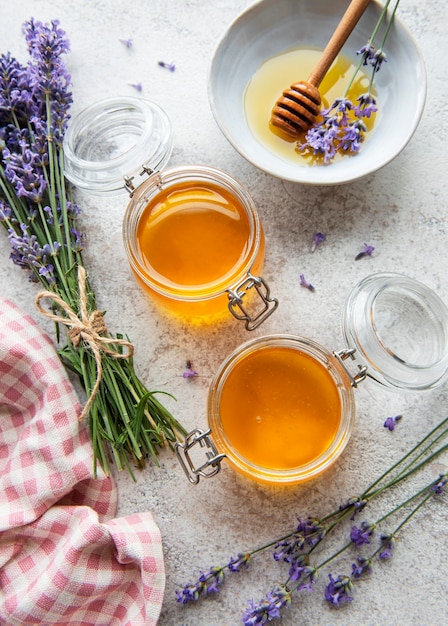 Jars with honey and fresh lavender flowers on a concrete background