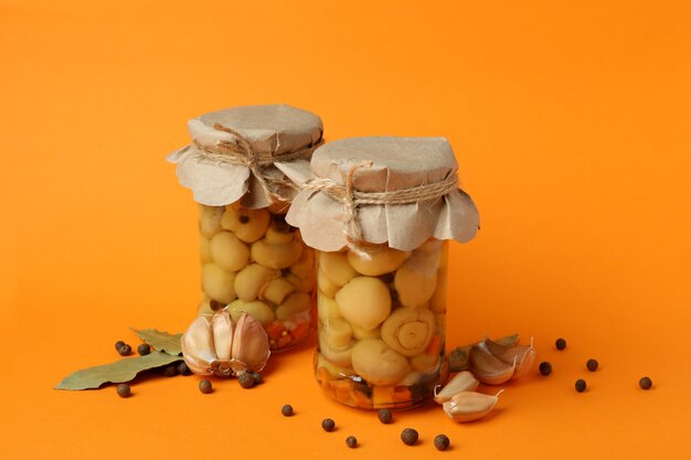 Jars with marinated mushrooms on orange background