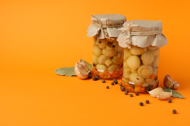 Jars with marinated mushrooms on orange background