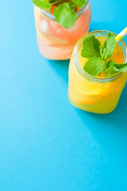 Jars with orange and grapefruit lemonade decorated ice and mint on blue paper background