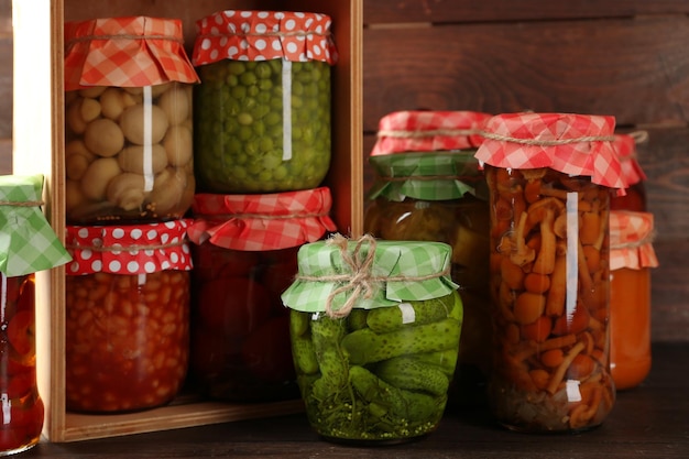 Jars with pickled vegetables and beans on wooden background