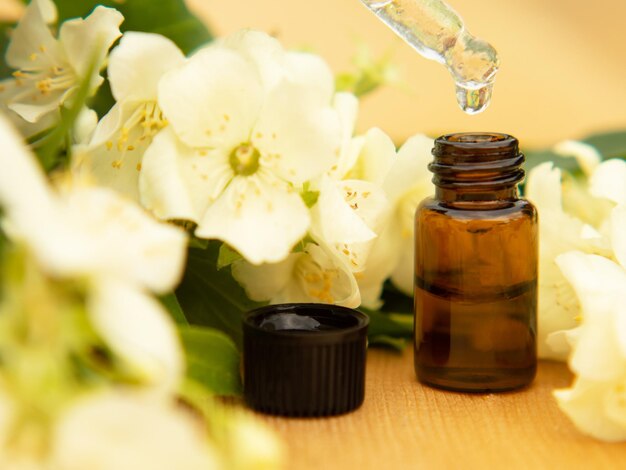 Jasmine essential oil in a glass bottle on a background of jasmine flowers on a wooden table