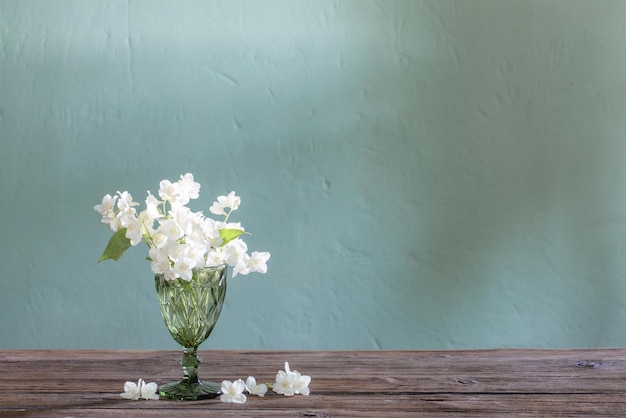 Jasmine flowers in glass vase on green background