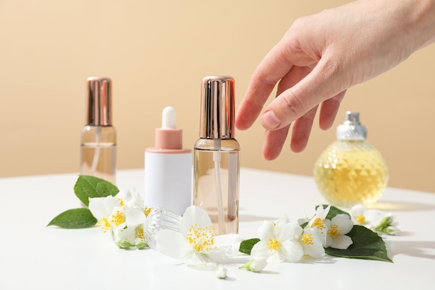 Jasmine flowers perfume bottles and female hand on beige background