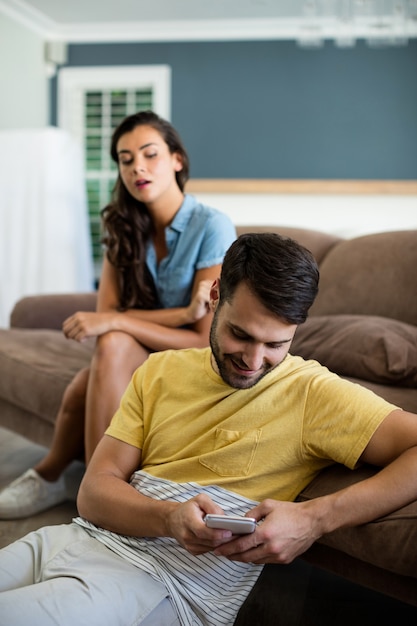 Jealous woman watching man using mobile phone in the living room at home