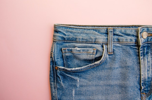 Jeans on a pink table. Jeans elements, pockets, seams in close-up. Ripped jeans.