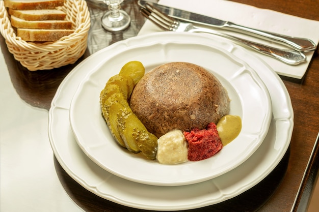 Jelly meat homemade, with cut canned cucumber, spices, mustard and bread serving in restaurant. Festive traditional north food.