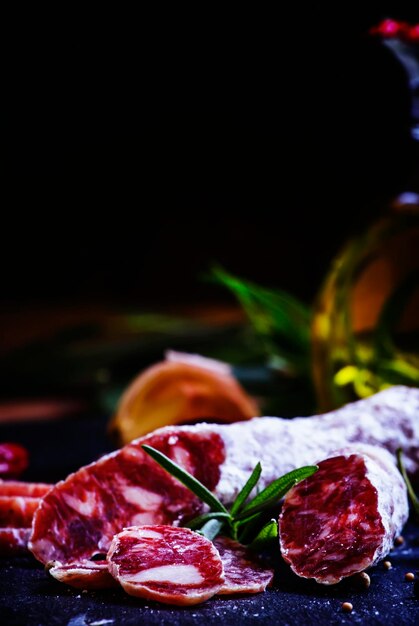 Jerked Italian salami with rosemary spices olives and oil Dark vintage background low key selective focus