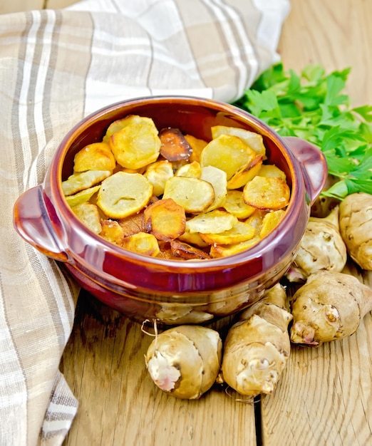 Jerusalem artichokes roasted in a clay pot, parsley, fresh artichoke tubers, napkin on a wooden board