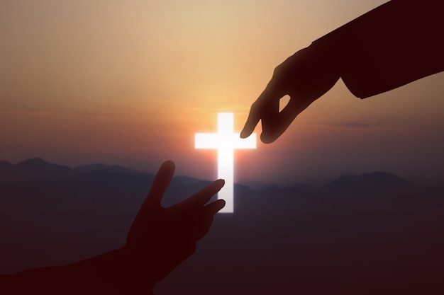 Jesus Christ giving a helping hand to human with a sunset sky background