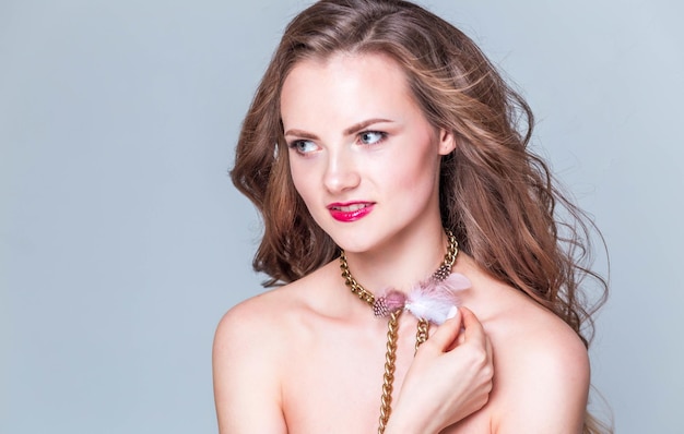 Jewelry from a chain of golden color white and pink bird fluff around the neck of a brunette girl Woman posing on a gray background in the studio looking away and smiling