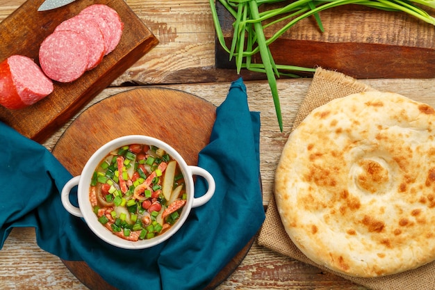 Jewish cuisine bean soup cholit on a blue napkin next to bread sausage and green onions