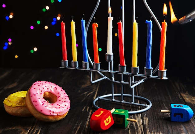 Jewish holiday Hanukkah background A traditional dish is sweet donuts Hanukkah table setting candlestick with candles and spinning tops on black background Lighting Chanukah candles Copy space