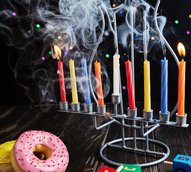 Jewish holiday Hanukkah background A traditional dish is sweet donuts Hanukkah table setting candlestick with candles and spinning tops on black background Lighting Chanukah candles Copy space