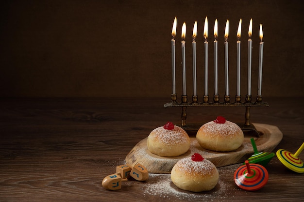 Jewish holiday Hanukkah concept and background. Hanukkah food doughnuts, candles and traditional spinning dreidel.