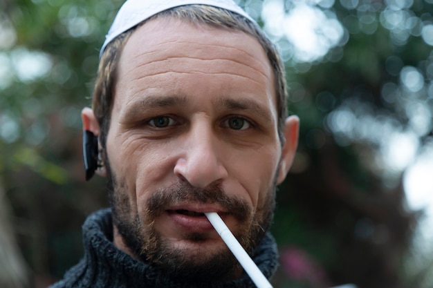 Jewish man wearing kippah bluetooth earpod and smoking a cigarette