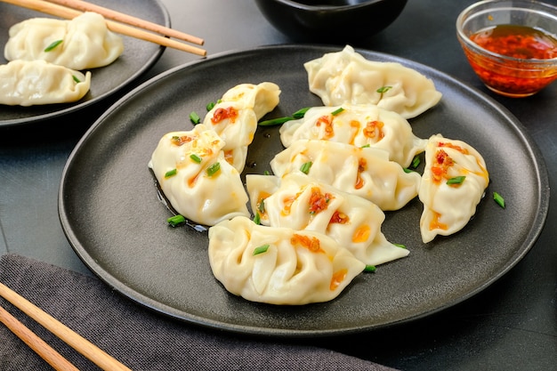 Jiaozi gyoza dumplings steamed on black plates with soy sauce and chili oil.