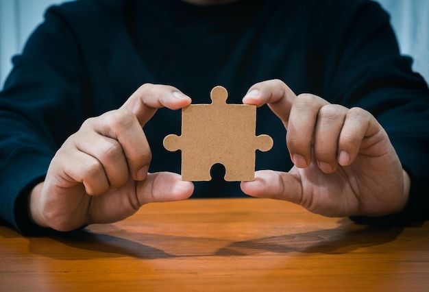 Photo a jigsaw puzzle holding businessmans hand person hands showing empty piece of important jigsaw puzzle on wood table business solution and idea partnership elements of career success part concept