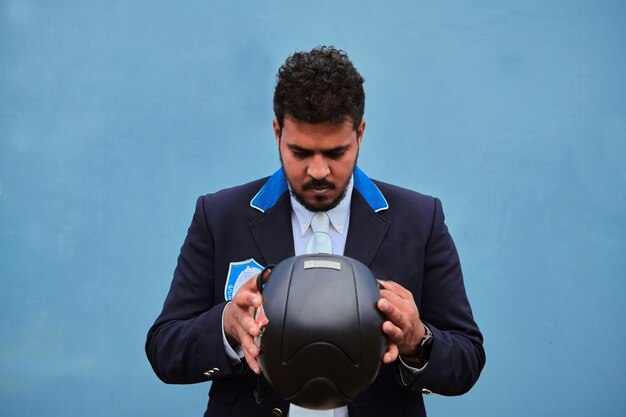 Jockey wearing uniform looking at his helmet before putting it on on a blue background