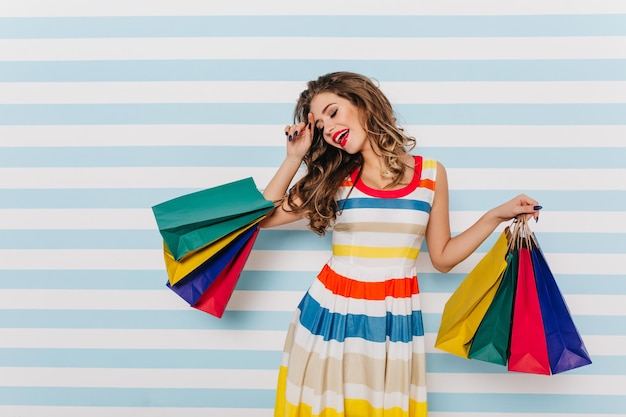 Jocund well-dressed girl enjoying summer shopping. Indoor photo of tired but smiling woman with paper bags.