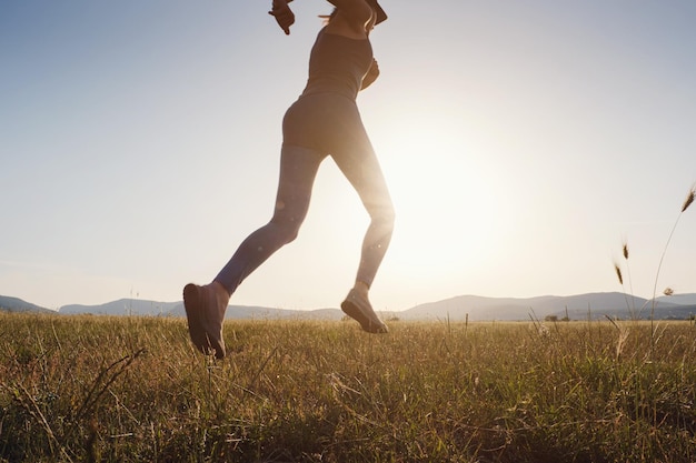 Jogging woman running in summer field at sunset