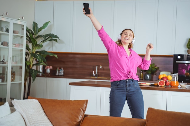 Join me. Pretty girl keeping smile on her face while dancing alone in the kitchen