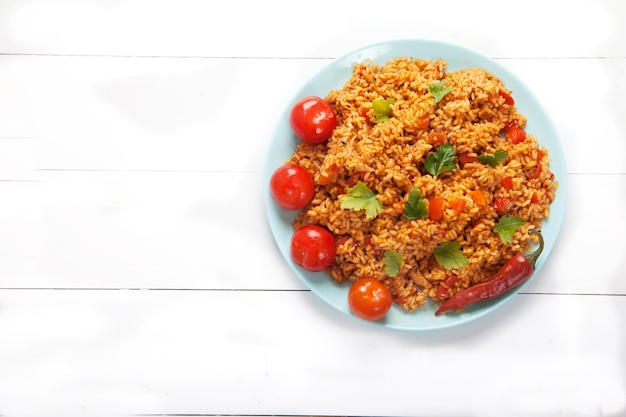 Jollof rice, tomatoes and hot peppers on a blue plate on a white background. National cuisine of Africa.