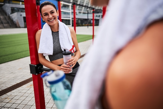 Jolly athletic female is standing on open sports ground and communicating with man after joint workout