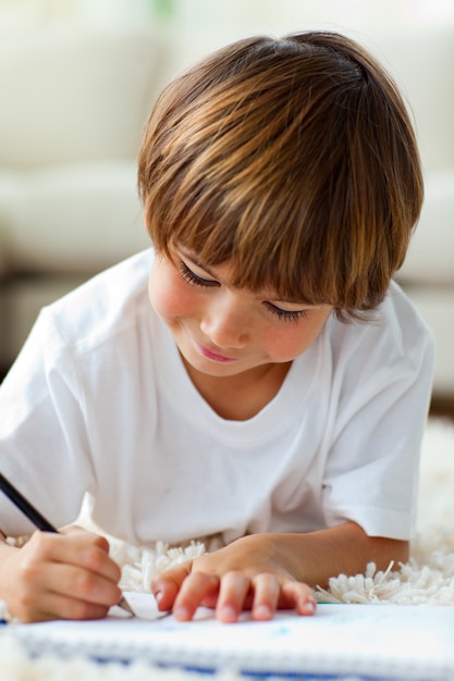 Jolly little boy drawing lying on the floor