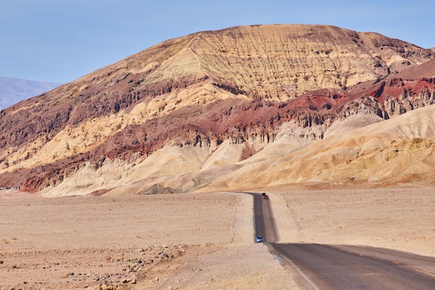 The journey down a long straight road in a desert leading to large colorful mountains