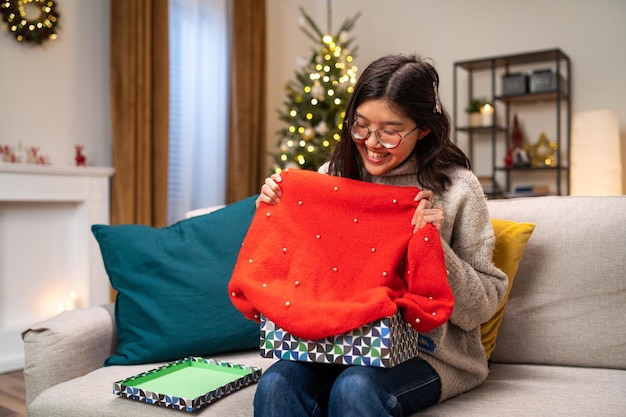 The joy of receiving a christmas gift a cheerful woman unwraps a winter red sweater from a box