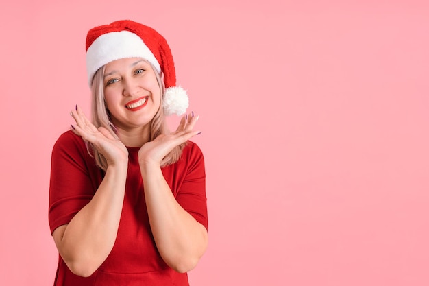 Joyful 40s woman in santa hat on pink background, copyspace