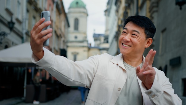 Joyful adult male tourist holding smartphone looking at screen taking pictures on webcam happy man