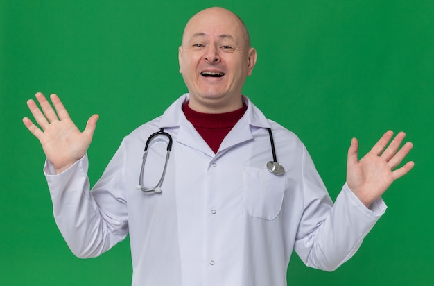 Joyful adult man in doctor uniform with stethoscope standing with raised hands 