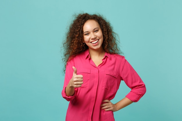 Joyful african american girl in casual clothes showing thumb up, looking camera isolated on blue turquoise wall background in studio. People sincere emotions, lifestyle concept. Mock up copy space.