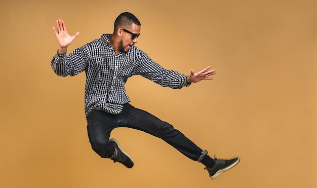 Joyful african american guy jumping or dancing isolated over beige background Indoor photo of stunning male model having fun in studio