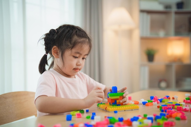 Joyful Asian girl happy and smiling playing colorful Lego toys sitting on the table in the living room creatively playing with Lego building colorful structures creativity imagine